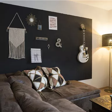 A stylish living area with a dark wall, decorative elements, and a cozy couch. A guitar and a lamp give the room an inviting atmosphere.