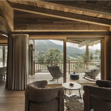 Ein modern eingerichtetes Zimmer mit Holzdecke und großen Fenstern. Der Blick auf die Berge und die Natur schafft eine gemütliche Atmosphäre.