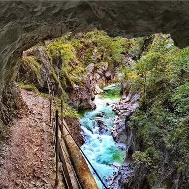 A view from a cave of a clear, turquoise river flowing through a rocky gorge. Surrounded by lush greenery and slate rocks, the landscape is breathtaking.