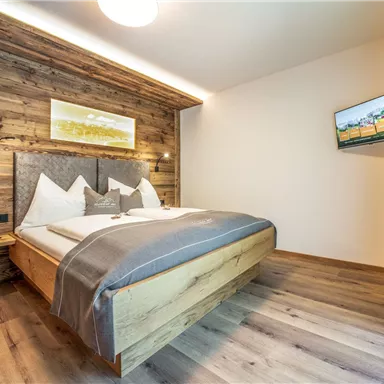 A modern room with a double bed and wooden panels. There is a flat-screen TV on the wall and the floor is made of wood.
