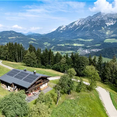 Ein malerisches Holzhaus mit Solarpanelen in den Bergen. Die Landschaft ist grün und üppig mit einem Blick auf majestätische Berge.