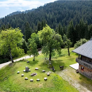 Eine malerische Landschaft mit einem Holzhaus und grünen Wiesen. Um das Haus herum stehen Bäume, und auf der Wiese gibt es einen Steinkreis.
