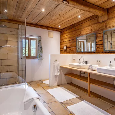 Ein modernes Badezimmer mit Holzverkleidung und zwei Waschbecken. Die Dusche ist durch eine Glasabtrennung getrennt und der Raum ist hell und einladend.