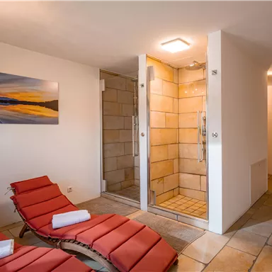 Ein modernes Badezimmer mit zwei Duschkabinen und roten Liegen. An der Wand hängt ein Bild von einem Sonnenuntergang am Wasser.