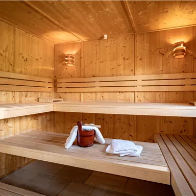 Eine helle Sauna mit Holzregalen und sanftem Licht. Handtücher und ein Holzbehälter stehen bereit.