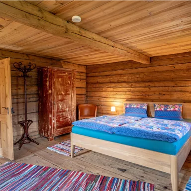 Ein gemütliches Schlafzimmer mitHolzdecke und Wänden. Das Zimmer verfügt über ein großes Bett, einen Stuhl und einen Kleiderschrank.