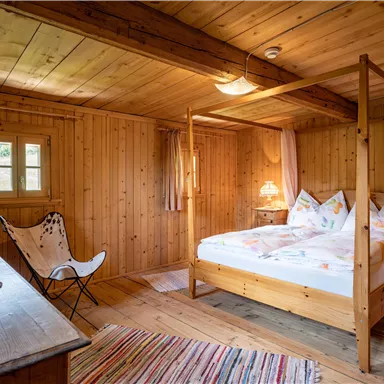 Ein gemütliches Schlafzimmer mit Holzwänden und einem Himmelbett. Der Raum ist warm und einladend, mit sanftem Licht und einfachen Möbeln.