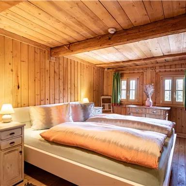 Ein gemütliches Schlafzimmer mit Holzwänden und zwei Betten. Sanfte Beleuchtung und grüne Vorhänge schaffen eine einladende Atmosphäre.