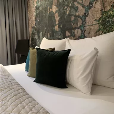 Ein modernes Schlafzimmer mit einem großen Bett und bunten Kissen. Die Wand ist mit einem künstlerischen Muster dekoriert.