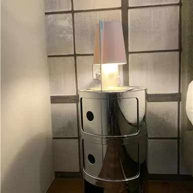 Ein moderner Nachttisch aus glänzendem Material mit drei Schubladen. Oben steht eine stilvolle Lampe mit einem farbigen Lampenschirm.