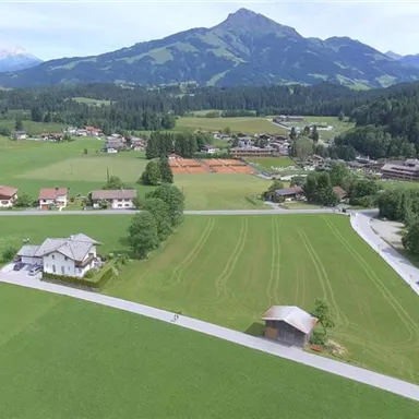 A picturesque landscape with green meadows and gentle hills. In the background, majestic mountains rise under a clear sky.