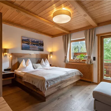 A cozy bedroom with a double bed and wooden ceiling. The room has large windows that let in plenty of natural light.