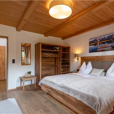 A cozy bedroom with a wooden ceiling and a large bed. The walls are light, and there is plenty of natural light.