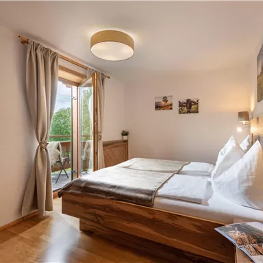 A cozy bedroom with two beds and natural wood decor. Large windows ensure plenty of daylight and offer a view of the outdoors.
