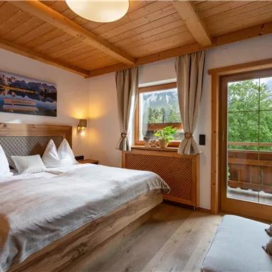 A cozy bedroom with a large double bed and wooden furniture. The window offers a view of the green landscape outside.