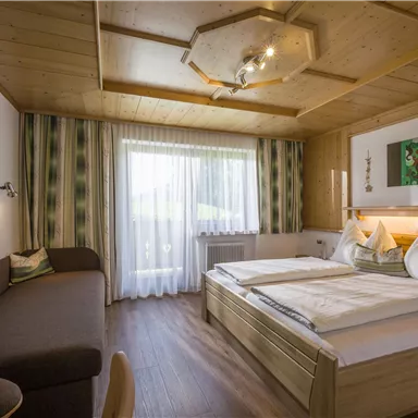 Ein gemütliches Schlafzimmer mit Holzdekor und zwei Betten. Große Fenster lassen viel Tageslicht herein und bieten einen Blick nach draußen.