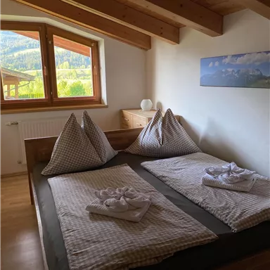 A cozy bedroom with a double bed and two large pillows. The windows offer a view of the surrounding nature.