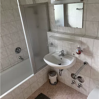 A modern bathroom with a shower, bathtub, and sink. The walls are tiled and there is a large mirror.