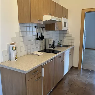 A modern kitchen with wooden cabinets and a bright countertop. It is equipped with basic kitchen appliances and tableware.