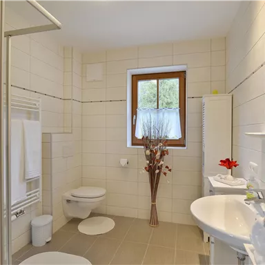 Ein modernes Badezimmer mit Dusche, Waschbecken und Toilette. Die hellen Fliesen und das Fenster schaffen eine einladende Atmosphäre.
