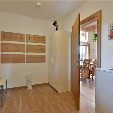 Ein heller Flur mit hellem Boden und weißen Möbeln. Auf der Wand hängen Holztafeln, und eine Tür führt zu einem Essbereich.