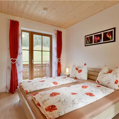 Ein modernes Schlafzimmer mit einem Doppelbett und roten Vorhängen. Große Fenster bieten einen Blick auf die Außenlandschaft.