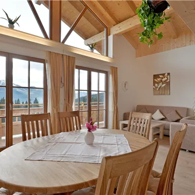Eine helle und moderne Wohnküche mit Holzdetails und großen Fenstern. Im Hintergrund sind Berge und ein gemütliches Sofa zu sehen.