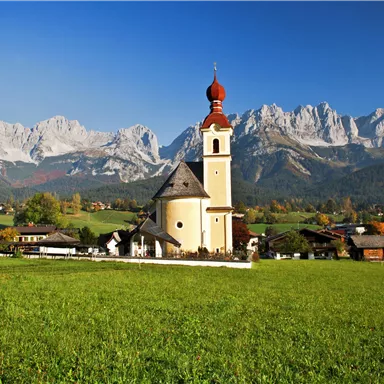 A picturesque church in the landscape with mountains in the background. Green meadows surround the attractive scenery.