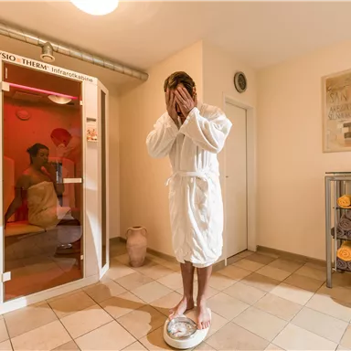 A relaxing wellness area with a man in a bathrobe standing on a scale. In the background, an infrared cabin is visible.
