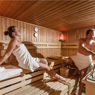 A modern sauna interior with wooden cladding. Two people relax in towels while enjoying the warmth.