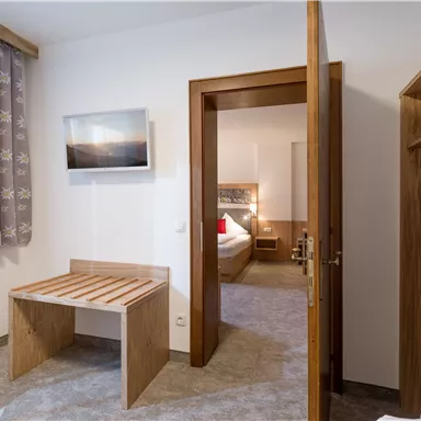 A cozy room with a wooden table and a chair. In the background, another room is visible that is modernly furnished.