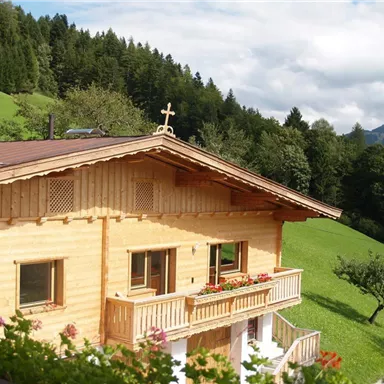 Ein gemütliches Holzhaus inmitten einer grünen Landschaft. Im Hintergrund sind Bäume und Berge zu sehen.
