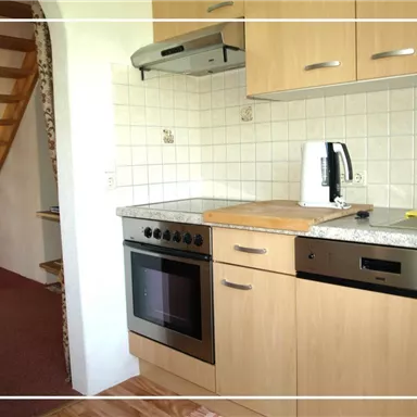 A modern kitchen with wooden cabinets, a stove, and a sink. In the background, a staircase is visible.