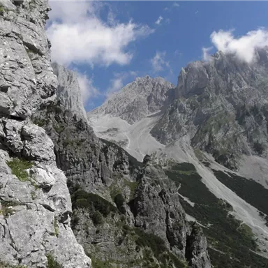 Eine beeindruckende Gebirgslandschaft mit steilen Felsen und hohen Gipfeln. Der Himmel ist teilweise bewölkt und zeigt eine Mischung aus blauem und grauem Licht.