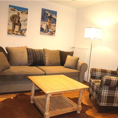 A cozy living room with a gray sofa and a checked armchair. Pictures hang on the wall, and a wooden table stands in the middle of the room.