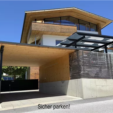 Ein modernes Haus mit Holz- und Betonelementen. Der überdachte Parkplatz lädt zum sicheren Parken ein.