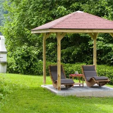 A pavilion in the garden with two lounge chairs and a small table. In the background, trees and a grill can be seen.
