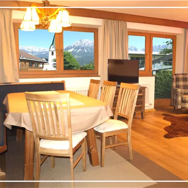 A cozy living area with a dining table and chairs. Through the windows, you can see a beautiful mountain landscape.