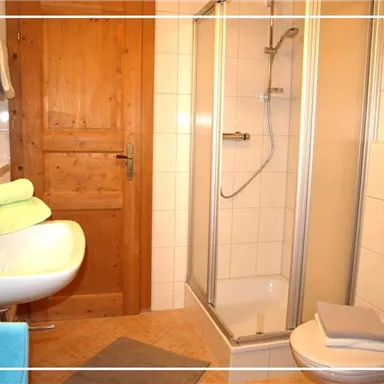 A modern bathroom with a shower and a sink. Colored towels are placed on the sink, and the walls are tiled in light colors.
