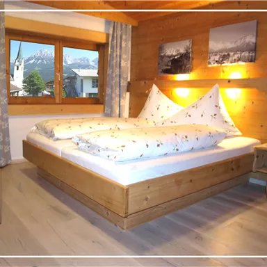 A cozy bedroom with a wooden bed and a large window. The walls are made of wood, and there are pictures on the wall.