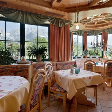 A cozy restaurant with wooden furniture and bright tables. Large windows provide a view of nature and the mountains.