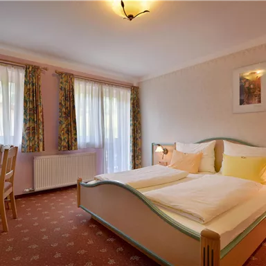 A cozy bedroom with a double bed, a table, and chairs. Large windows provide plenty of daylight and an inviting atmosphere.