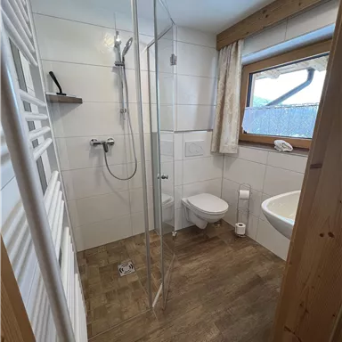 Ein modernes Badezimmer mit Dusche und Badewanne. Helle Fliesen und Holzdetails sorgen für eine gemütliche Atmosphäre.