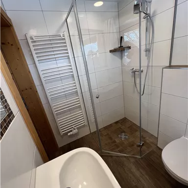 Ein modernes Badezimmer mit einer gläsernen Duschkabine und einer Badewanne. Die Wände sind hell gefliest, und es gibt einen Handtuchwärmer.