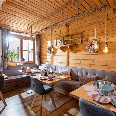 A cozy restaurant with wooden paneling and warm light. The tables are lovingly set, and the windows offer a view outside.