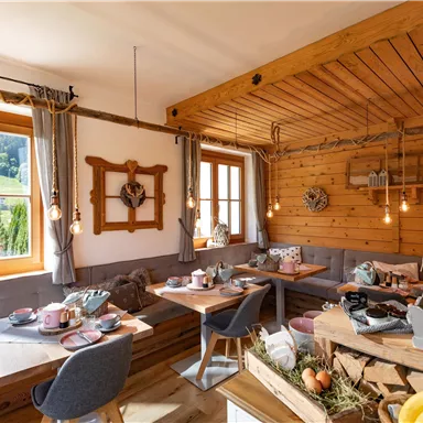 A cozy room with wooden walls and large windows. It is lovingly furnished and offers a table with breakfast and snacks.