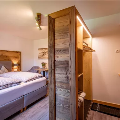 A cozy bedroom with a double bed and warm wooden furniture. A wardrobe and decorative elements create an inviting atmosphere.