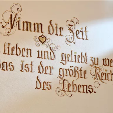 A beautifully designed inscription on the wall. It reads: "Take time to love and be loved; that is the greatest wealth of life."