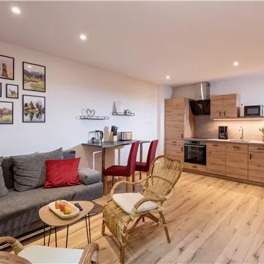 A modern living room with a comfortable sofa and a dining table. The decor is bright and inviting, with pictures on the wall and a kitchenette.