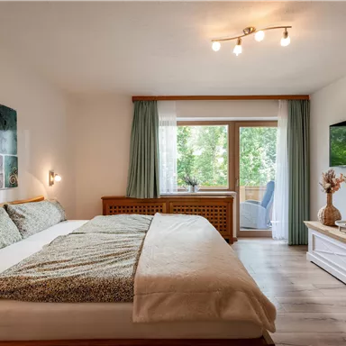 A bright bedroom with a large bed and warm colors. A view of greenery is possible through the window.